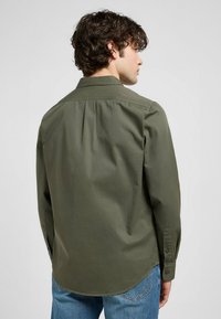 Olijfgroene lange mouwen shirt, van katoen, aansluitende pasvorm, afgeronde zoom, enkele plooit aan de achterkant, verstelbare knoopmanchetten, minimalistisch ontwerp.