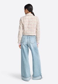 Giacca in tweed bianco con quadri colorati, abbinata a jeans a gamba larga azzurri chiari con orli sfrangiati e una vestibilità rilassata.