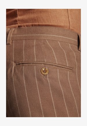 Braune Nadelstreifenhose mit einer geknöpften Gesäßtasche, getragen mit einem passenden braunen Gürtel und Hemd.