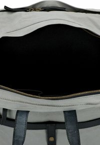 Interno di una borsa in tessuto grigio con fodera nera, chiusura con cerniera, denti dorati e manici in pelle nera. Design minimalista, senza dettagli esterni visibili.