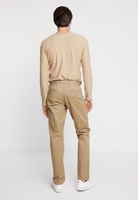 Chino khaki con taglio dritto, dotati di tasche posteriori, abbinati a una camicia a maniche lunghe color sabbia e sneakers bianche. Tessuto dalla consistenza liscia.