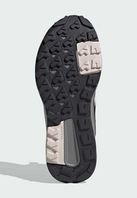 Černá guma podešev boty s texturovanými vzory a světlými šedými akcenty. Obsahuje trojúhelníkové a obdélníkové vzorky pro zvýšení přilnavosti. Text zní "TRAXION."