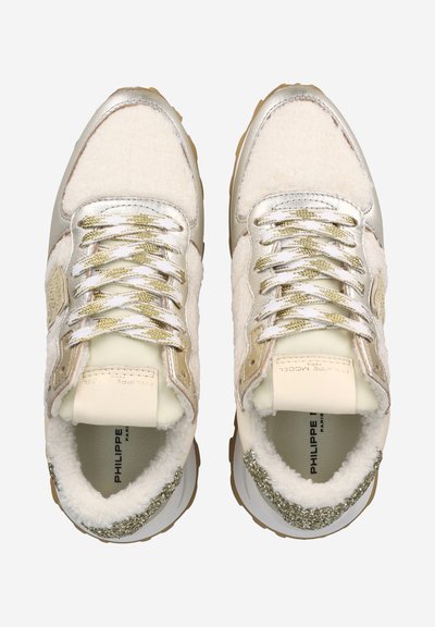 White and gold sneakers featuring a textured fur-like upper, metallic accents, and a sturdy rubber sole. Lace-up design with patterned laces.