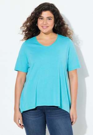 T-shirt turquoise à manches courtes avec un col en V et un ourlet légèrement évasé. Texture douce et lisse. Porté avec un jean bleu foncé.
