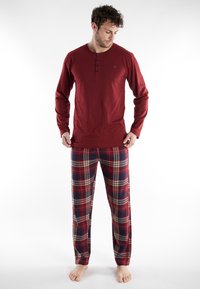 Rode longsleeve shirt met een geknoopte kraag, gecombineerd met geruite broek met rode, marineblauwe en crèmekleurige strepen. Zachte stof, relaxed fit.