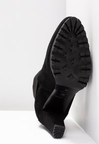 Černé semišové kotníkové boty s texturovanou černou gumovou podrážkou. Nabízí elegantní design a vyztuženou patu pro stabilitu.