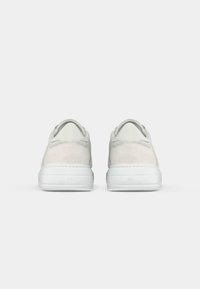 White sneakers with a smooth leather upper and suede accents, featuring a round toe, low-profile sole, and minimalistic design.