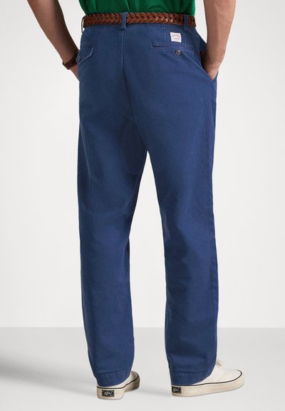 Blå bomulls-chinos med avslappnad passform, utrustade med bakfickor, ett vävt brunt bälte och cremefärgade skor. Subtila textur- och designdetaljer synliga.
