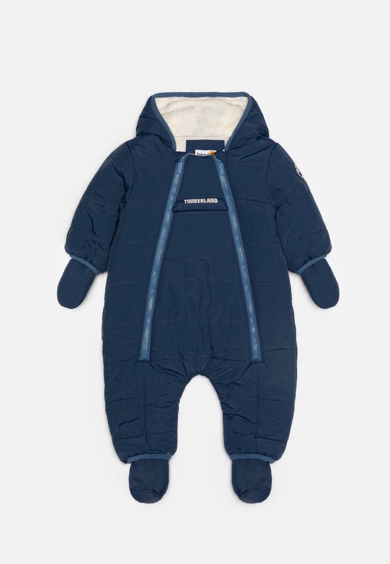 Combinaison de neige matelassée pour bébé de couleur bleu marine, avec capuche, moufles, chaussons, deux fermetures éclair à l'avant, et logo Timberland sur la poitrine.