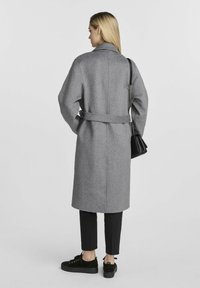 Szary wełniany płaszcz z paskiem w talii, kołnierzem szala i opuszczonymi ramionami; zestawiony z czarnymi spodniami i sneakerami; elegancki, minimalistyczny design.