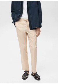 Světlé béžové kalhoty s pásem na stahování, slim fit a bočními kapsami, spárované s tmavou košili na knoflíky a černými sandály.