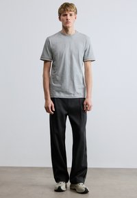 Szürke rövid ujjú póló kontrasztos csíkokkal a mandzsettákon, laza fekete nadrággal és világos árnyalatú tornacipővel párosítva.