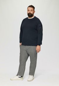 Granatowy sweter z okrągłym dekoltem o teksturowanej powierzchni, szare spodni w kratę i białe trampki z subtelnym akcentem. Casualowy krój.