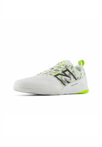 White athletic shoe with mesh upper, green accents, and textured sole. Features perforated design and bold branding on the side.
