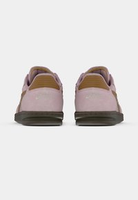 Calçado com um cabedal em camurça rosa, pormenores em castanho, detalhes texturizados no calcanhar e uma sola de borracha escura. Logótipo refletivo na lateral.