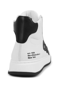 Zapatillas altas de cuero blanco con detalles en negro. Presentan un cuello y un talón acolchados, logo lateral texturizado y detalles de marca impresos.