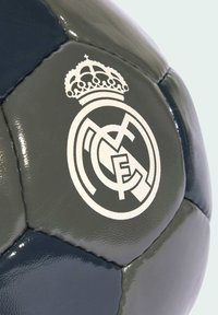 Balón de fútbol gris y marino con un acabado brillante, logotipo en relieve del Real Madrid con corona y paneles hexagonales cosidos.