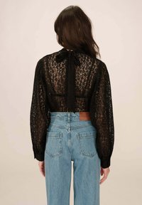 Zwarte kanten top met lange mouwen en een hoge halslijn, met een strik aan de achterkant, gecombineerd met lichtblauwe high-waisted jeans. Gekoze stof en een losse pasvorm.