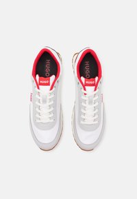 Weiße Sneaker mit grauen Akzenten, roter Fütterung und strukturiertem Gummisole. Verfügt über Schnürsenkel und "HUGO"-Branding auf der Zunge und der Seite.