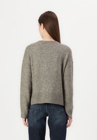 Grå strikket genser med avslappet passform, senket skuldre, ribbestrikket kant og litt cropped lengde, kombinert med mørk denim jeans.