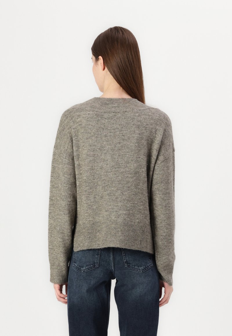Pull en tricot gris avec une coupe décontractée, épaules tombantes, ourlet côtelé et longueur légèrement raccourcie, associé à un jean en denim foncé.
