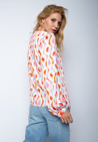 Langärmlige Bluse aus leichtem Stoff mit einem mehrfarbigen Wellenmuster. Sie hat einen lockeren Schnitt und elastische Bündchen und wird mit heller Denim kombiniert.