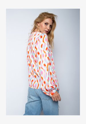 Bluzka z długim rękawem z lekkiego materiału w wielokolorowy wzór fal. Posiada luźny krój i elastyczne mankiety, zestawiona z jasnymi dżinsami.