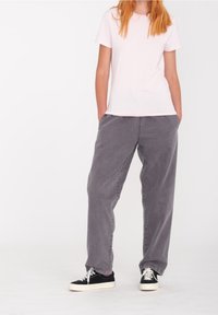 Vaaleanpunainen puuvillainen t-paita yhdistettynä väljälahkeisiin harmaisiin farkkuihin. Asun täydentävät mustavalkoiset tennarit.