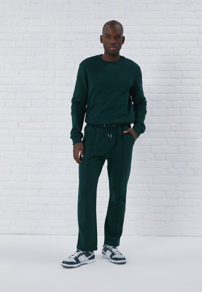 Mørkegrøn sweatshirt og matchende joggers med snor. Sættet har ribbede manchetter og sidesømme. Sammen med sorte og hvide sneakers.