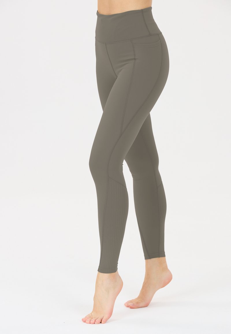 Hochtaillierte Leggings in olivgrün, aus einem glatten Material mit auffälligen Seitennähten und gerippten Akzenten an den Unterschenkeln.