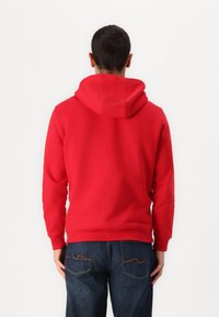 Felpa con cappuccio rossa realizzata in misto cotone, con tasca a marsupio e polsini a coste. Indossata con jeans in denim scuro.