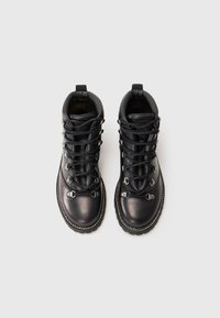 Par de botas de caminhada pretas de couro, com colarinhos acolchoados, ilhós de metal e atacadores pretos, mostradas de vista superior sobre um fundo branco liso.