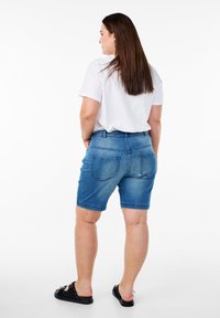 Shorts de denim en un lavado medio con una cintura ajustada, dos bolsillos traseros y un dobladillo justo por encima de la rodilla, combinados con una camiseta blanca.