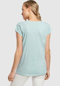 Lyseblå t-shirt med rullede korte ærmer, let løs pasform og buet kant. Blødt bomuldsstof, minimalistisk design.