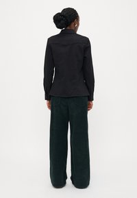 Zwarte langekiel met een kraag, gecombineerd met hoge taille, wijde donkergroene corduroy broek. Soepele stoftextuur en gedetailleerde stiksels.