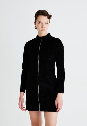 Abito in corduroy nero con colletto e maniche lunghe. Presenta una zip frontale e una silhouette aderente con dettagli cuciti.
