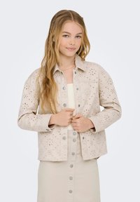 Šviesiai smėlio spalvos švarkas su gėlių išpjovomis, mygtukų užsegimu ir dviem krūtinės kišenėmis. Suporuotas su atitinkamu šviesiai smėlio spalvos sijonu.