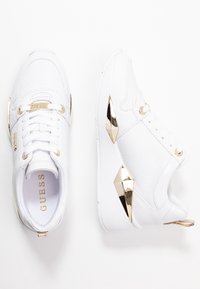 Weißes Sneaker-Modell mit strukturiertem Design, goldenen Akzenten an den Ösen und der Ferse, chunky Form und robuster Sohle.