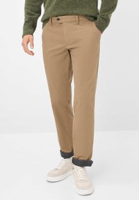 Khakifarbene Chinos mit geradem Bein, ausgestattet mit einem Knopfverschluss, seitlichen Taschen und hochgekrempelten Säumen über weißen Sneakers.