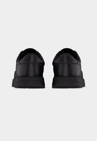 Ζευγάρι μαύρα παπούτσια χαμηλού τύπου με χοντρές σόλες, εμφανιζόμενα από την πίσω πλευρά σε απλό λευκό φόντο.