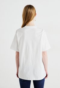 Weißes Baumwoll-T-Shirt mit kurzen Ärmeln und rundem Ausschnitt, in lässiger Passform und schlichter Gestaltung, von hinten gezeigt.