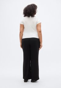 Λευκό κοντομάνικο τοπ συνδυασμένο με μαύρο παντελόνι φαρδιάς γραμμής. Λείο ύφασμα με εφαρμοστή κοπή, απεικονιζόμενο από πίσω. Απλός σχεδιασμός και καθαρή σιλουέτα.