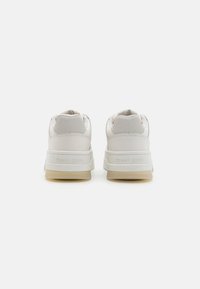 Valkoiset nahkasneakerit, joissa on sileä pinta, varustettuna pehmustetulla nilkkaremmillä ja vaalealla kumipohjalla. "TOMMY JEANS" -logo on kaiverrettu kantapäähän.