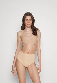 Sutiã wireless bege com copas lisas e moldadas e alças finas, combinado com calcinha de cintura alta sem costuras em tom nude correspondente.