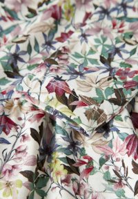 Floral fabric with detailed stitching, featuring leaves and flowers in green, purple, red, and beige on a white background.