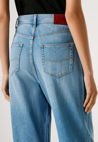 Vaqueros de mezclilla azul claro con cintura alta, que cuentan con dos bolsillos traseros y una etiqueta de marca de cuero rojo en la cintura.