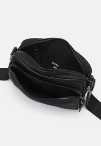 Borsa a tracolla nera in pelle con numerosi scomparti con zip e una tracolla in tessuto con logo, texture liscia e forma strutturata.