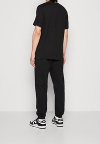 Black cotton t-shirt with a relaxed fit and short sleeves, paired with black sweatpants and black-and-white sneakers.