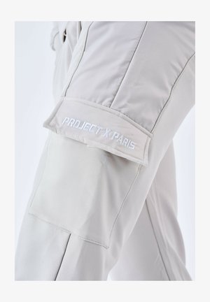 Pantalon gris clair avec une texture lisse. Présente une poche cargo sur la cuisse avec "PROJECT X PARIS" brodé en blanc. Design épuré.