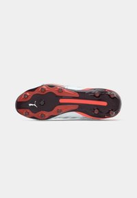 Soccer cleat with a textured black and red outsole, featuring prominent studs and a sleek, metallic silver upper. Puma logo visible.